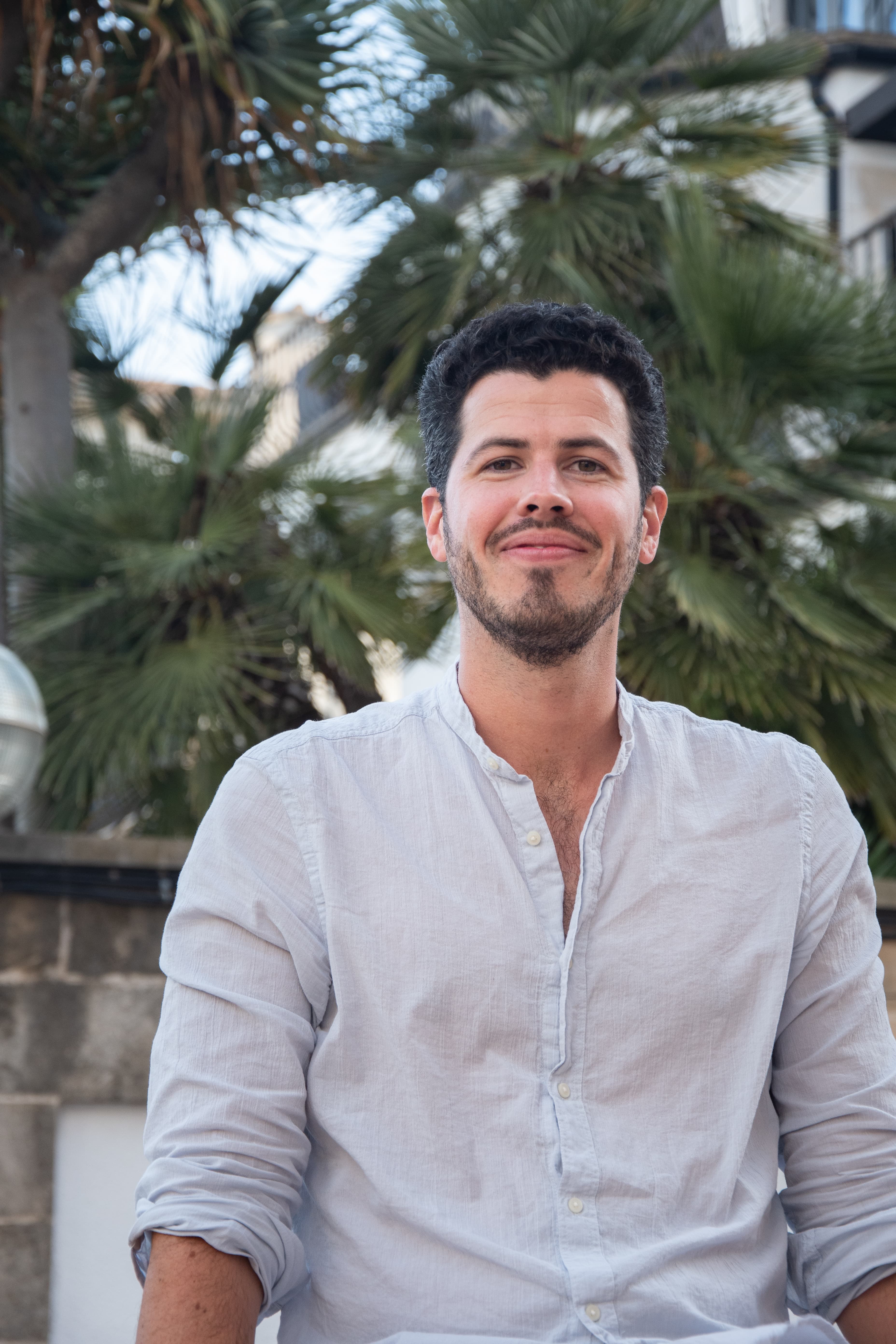 Smiling man with dark hair and beard wearing a light linen shirt with palm trees.