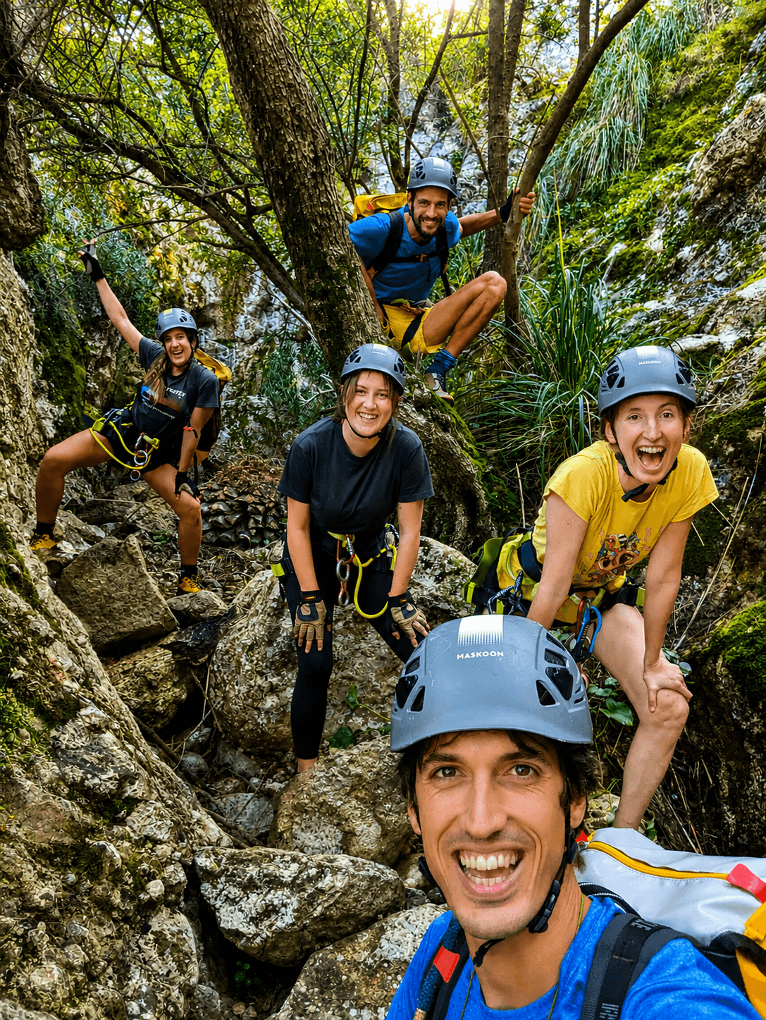Five smiling climbers in helmets and harnesses pose for a selfie in a rocky canyon.
