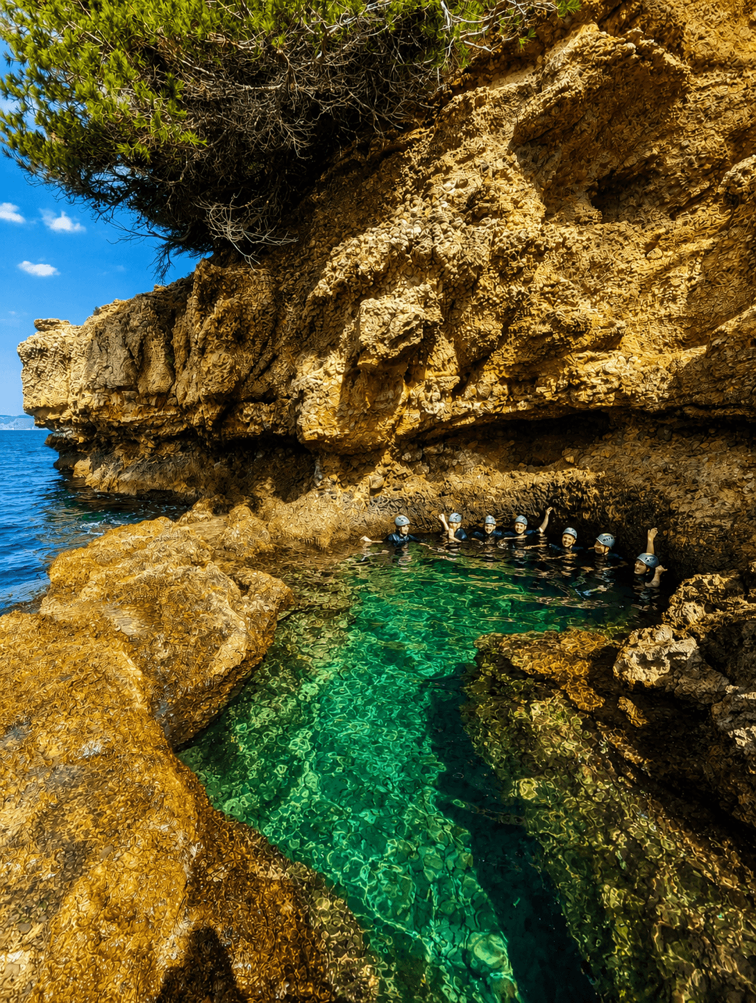 A group wearing helmets floats in clear turquoise water within a rugged, golden sea cave.